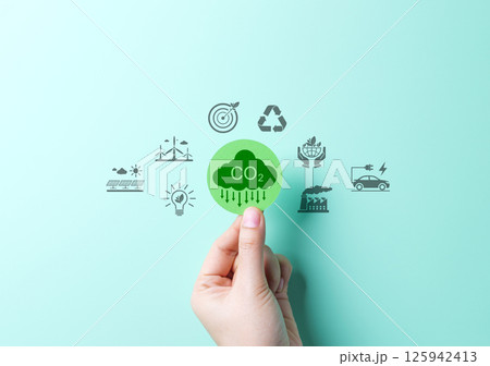 Reducing CO2 Emissions and Promoting Sustainability Concept. A hand holds green CO2 cloud icon with environmental symbols, such as solar, wind turbines, and recycling. Reduce carbon and go green. Reducing CO2 Emissions and Promoting Sustainability Concept. A hand holds green CO2 cloud icon with environmental symbols, such as solar, wind turbines, and recycling. Reduce carbon and go green. 125942413