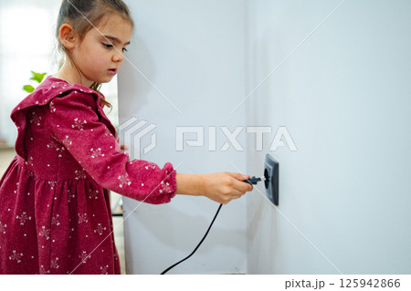 Young girl exploring electricity by plugging in a device in a cozy indoor space during daylight Young girl exploring electricity by plugging in a device in a cozy indoor space during daylight 125942866