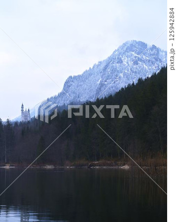 Majestic castle reflected in calm lake surrounded by snow-capped mountains and tall pine trees in winter Majestic castle reflected in calm lake surrounded by snow-capped mountains and tall pine trees in winter 125942884