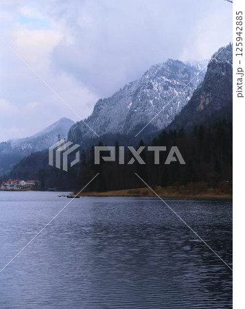 Scenic winter view of snow-covered mountains and tranquil lake at dawn with small village nestled by the shore Scenic winter view of snow-covered mountains and tranquil lake at dawn with small village nestled by the shore 125942885