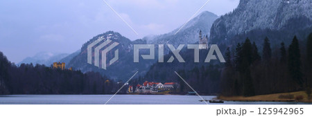 Majestic mountains surround a serene lake with a historic castle nestled in the landscape during twilight hours 125942965