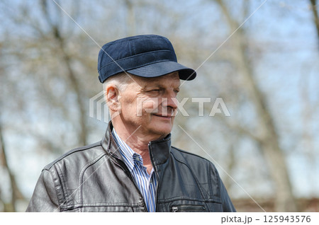 Gray-haired man in a blue cap and leather jacket. Old man in shirt and jacket on the street. Gray-haired man in a blue cap and leather jacket. Old man in shirt and jacket on the street. 125943576
