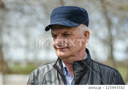 Pensioner in a hat with a visor, jacket and shirt on the street. In sunny weather, the pensioner is smiling and enjoying life. Pensioner in a hat with a visor, jacket and shirt on the street. In sunny weather, the pensioner is smiling and enjoying life. 125943582