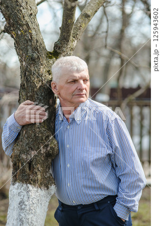 An old man is having a rest in the park. A pensioner near a tree smiles beautifully. An old man is having a rest in the park. A pensioner near a tree smiles beautifully. 125943602