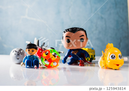 A yellow plastic fish and a colored ball lie on a flat surface. 125943814