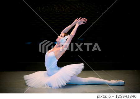 Ballet dancer in dramatic split pose with arms raised on theater stage 125943840
