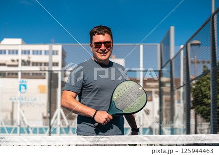 Man enjoying a sunny day of padel tennis on an outdoor court. Man enjoying a sunny day of padel tennis on an outdoor court. 125944463