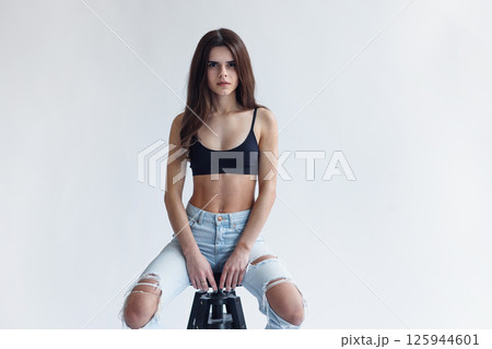 Charming skinny beautiful girl with perfect abs in jeans and black top isolated on gray background Charming skinny beautiful girl with perfect abs in jeans and black top isolated on gray background 125944601