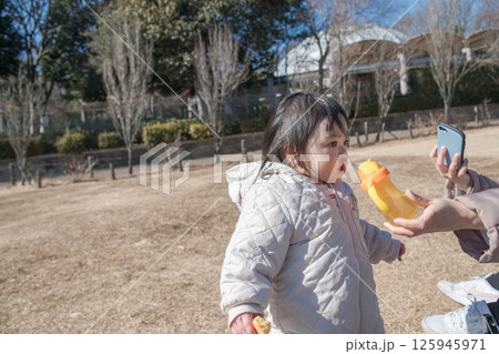 【相模原市立麻溝公園の芝生広場で遊ぶ1歳児とおかあさん　水分補給】 125945971