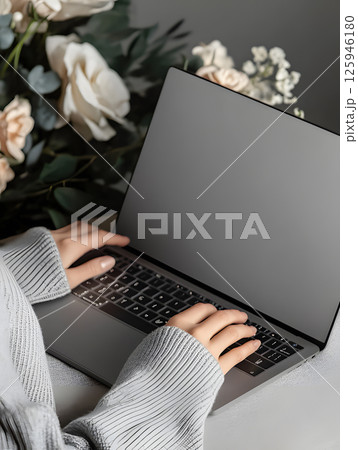 An open laptop stands on table with hands. Dark background. Side view. Computer mockup for design 125946180