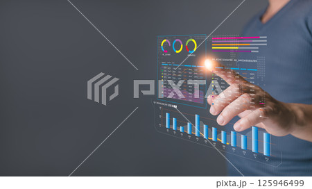 A person interacts with a glowing virtual dashboard displaying analytics and charts, emphasizing data analysis, business insights, and modern technology for decision making and performance tracking. 125946499