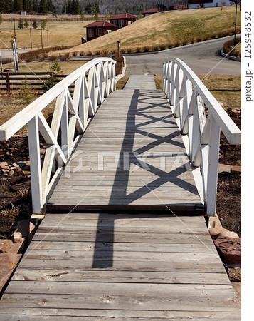 wooden bridge over pathway in scenic countryside area with grass and rustic buildings nearby. wooden bridge over pathway in scenic countryside area with grass and rustic buildings nearby. 125948532