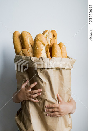 Child holding large paper bag filled with french baguettes against plain background 125950093