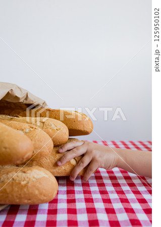 Child hand reaching for fresh baguettes on red checkered tablecloth Child hand reaching for fresh baguettes on red checkered tablecloth 125950102