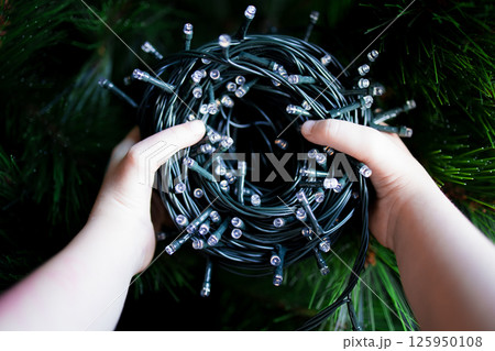 Childs hands holding twinkling Christmas string lights amidst greenery Childs hands holding twinkling Christmas string lights amidst greenery 125950108