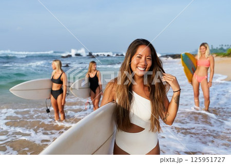 Group of women with surfboards on tropical beach. Smiling female surfers in swimsuits ready for surfing adventure. Ocean waves, clear sky create perfect vacation. Active lifestyle, summer fun. Group of women with surfboards on tropical beach. Smiling female surfers in swimsuits ready for surfing adventure. Ocean waves, clear sky create perfect vacation. Active lifestyle, summer fun. 125951727