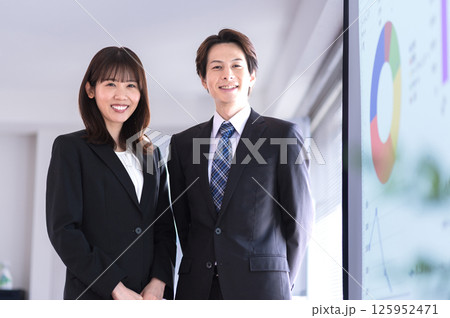 会議室のスクリーンの前に立つスーツ姿の男女 会議室のスクリーンの前に立つスーツ姿の男女 125952471