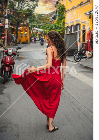 back of a young beautiful female tourist traveler in a red dress on the street in old town in Hoi An in Vietnam in Asia 125952647