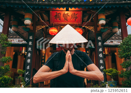 male tourist in Vietnamese Non La hat prays at temple on a Buddhist pagoda in Vietnam in Asia male tourist in Vietnamese Non La hat prays at temple on a Buddhist pagoda in Vietnam in Asia 125952651