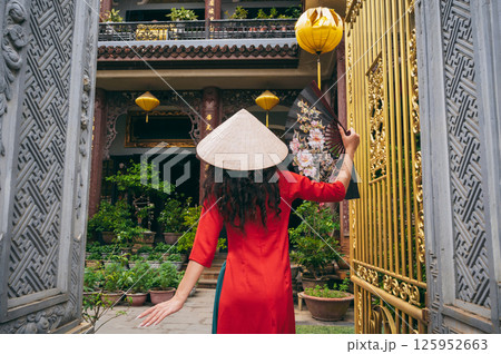 back of a female traveler tourist in a Vietnamese hat at Buddhist temple in Hoi An in Vietnam in Asia 125952663