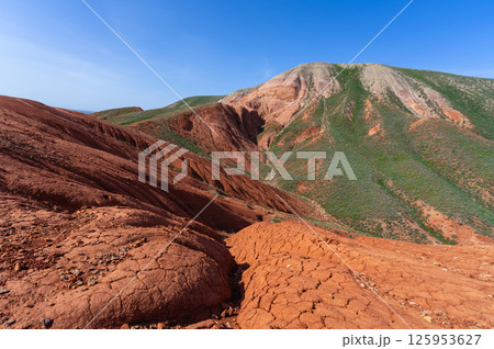 Red clay and green slopes under a blue sky in the mountains Red clay and green slopes under a blue sky in the mountains 125953627