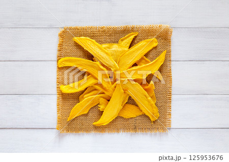 Dried mango slices displayed on a square piece of burlap over a white wooden table in flat lay style 125953676