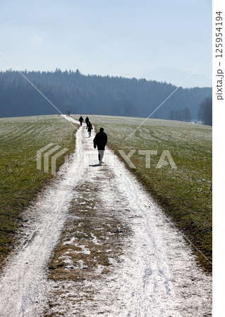 A group of people are walking down a path in a snowy field A group of people are walking down a path in a snowy field 125954194