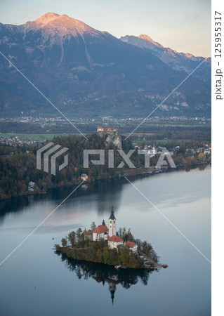 Vertical alpine scenery with lake, island and church in the middle and mountain peaks in backdrop Vertical alpine scenery with lake, island and church in the middle and mountain peaks in backdrop 125955317