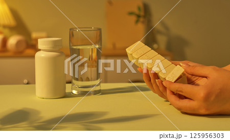 Hands are opening the bottom drawer of the daily medicine jar to take the medicine. A glass of water and a medium sized medicine bottle with a tight lid are placed on the table. Healthcare concept. Hands are opening the bottom drawer of the daily medicine jar to take the medicine. A glass of water and a medium sized medicine bottle with a tight lid are placed on the table. Healthcare concept. 125956303