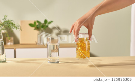 The cylindrical bottle has a transparent shell, white cap and can see the fish oil capsules inside. The yellow pills are filled with vitamins, omegas and other healthy nutrients. Indoor scene. 125956309