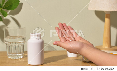Several brown vitamin capsules are placed in the palm of a hand. The hand turned towards the camera. A white pill bottle is placed on the table, open and without a label. White background. 125956332