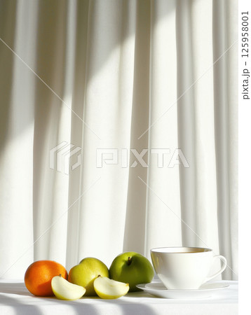Simple breakfast scene featuring cup of tea alongside fresh fruits, illuminated by soft sunlight 125958001