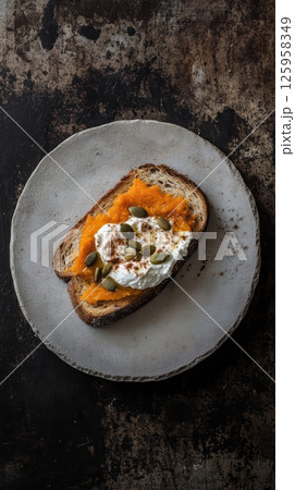 Rustic ceramic plate holding artisan toast spread with ricotta, topped by smooth pumpkin puree, sprinkled with pumpkin seeds and cinnamon against textured surface Rustic ceramic plate holding artisan toast spread with ricotta, topped by smooth pumpkin puree, sprinkled with pumpkin seeds and cinnamon against textured surface 125958349