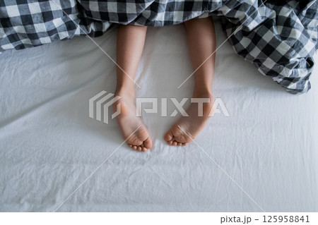 Child feet peeking from under checkered blanket on white bed Child feet peeking from under checkered blanket on white bed 125958841