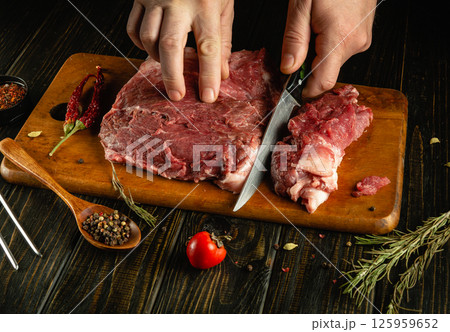 Hands skillfully cut raw meat on a wooden board surrounded by fresh spices and herbs, creating an inviting atmosphere in a traditional kitchen Hands skillfully cut raw meat on a wooden board surrounded by fresh spices and herbs, creating an inviting atmosphere in a traditional kitchen 125959652