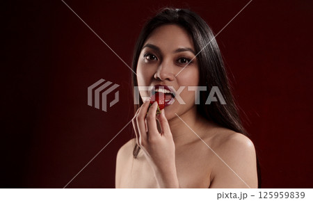 Beautiful Asian Woman Eating a Strawberry on Red Background Beautiful Asian Woman Eating a Strawberry on Red Background 125959839