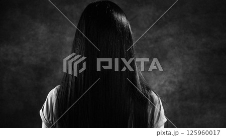 Woman with long black hair hiding her face in studio shot Woman with long black hair hiding her face in studio shot 125960017