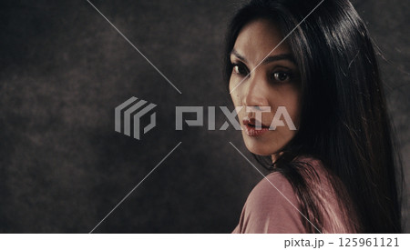 Serious young woman with long black hair looking over her shoulder 125961121