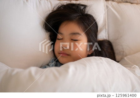 優しい光に包まれた寝室で布団に包まれて安心して眠る女の子 125961400