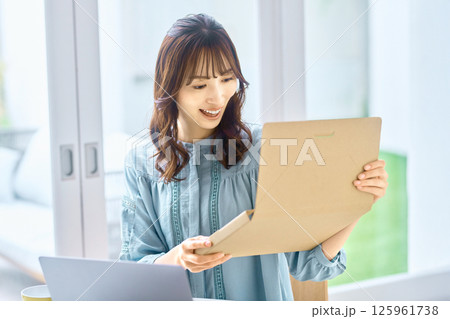 パソコンを見ながら荷物の確認をする若い女性 125961738