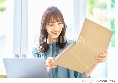パソコンを見ながら荷物の確認をする若い女性 パソコンを見ながら荷物の確認をする若い女性 125961743