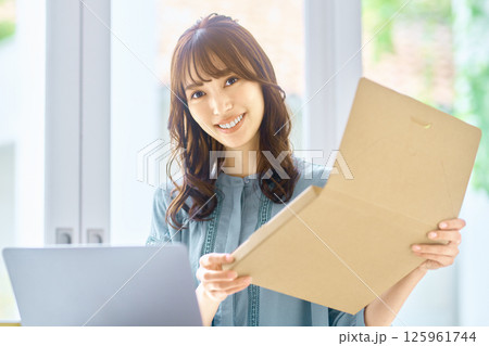 パソコンを見ながら荷物の確認をする若い女性 125961744