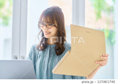 パソコンを見ながら荷物の確認をする若い女性 パソコンを見ながら荷物の確認をする若い女性 125961746