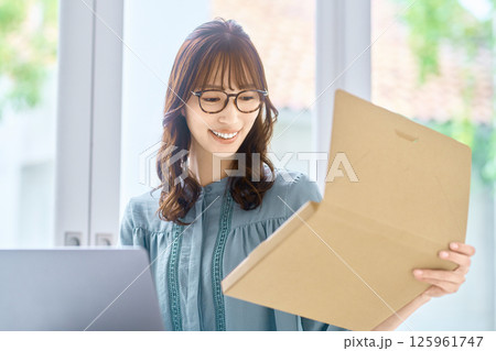 パソコンを見ながら荷物の確認をする若い女性 パソコンを見ながら荷物の確認をする若い女性 125961747