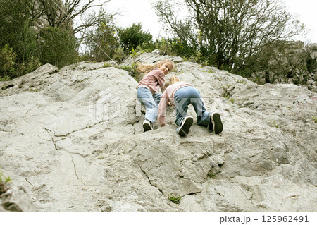 two little girls sisters twins climbing on rock together outside 125962491