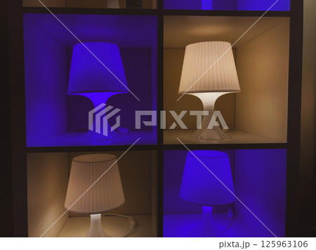 Four modern lamps, lamp shades are lighting in darkness. Contemporary home interior details. Lights in a dark. Deep purple blue and yellow lights wall 125963106