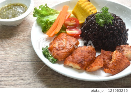 grilled slice pangasius dory fish on black riceberry with pumpkin carrot lettuce and tomato on plate dipping Thai spicy seafood sauce grilled slice pangasius dory fish on black riceberry with pumpkin carrot lettuce and tomato on plate dipping Thai spicy seafood sauce 125963256