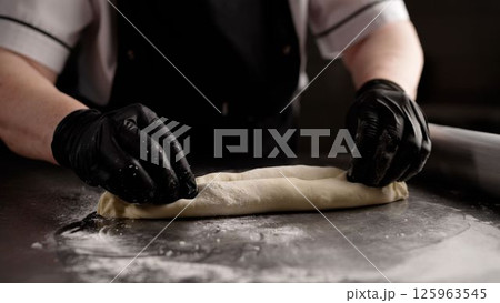 Chef rolling dough with rolling pin on stainless steel table 125963545