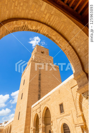 Arch view to minaret tower of the Great Mosque of Uqba with clouds in the blue sky, Kairouan 125963893