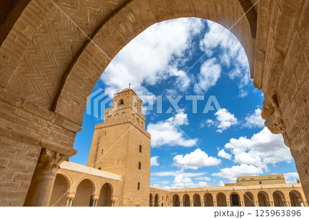 Arch view to minaret tower of the Great Mosque of Uqba with clouds in the blue sky, Kairouan, Tunis Arch view to minaret tower of the Great Mosque of Uqba with clouds in the blue sky, Kairouan, Tunis 125963896